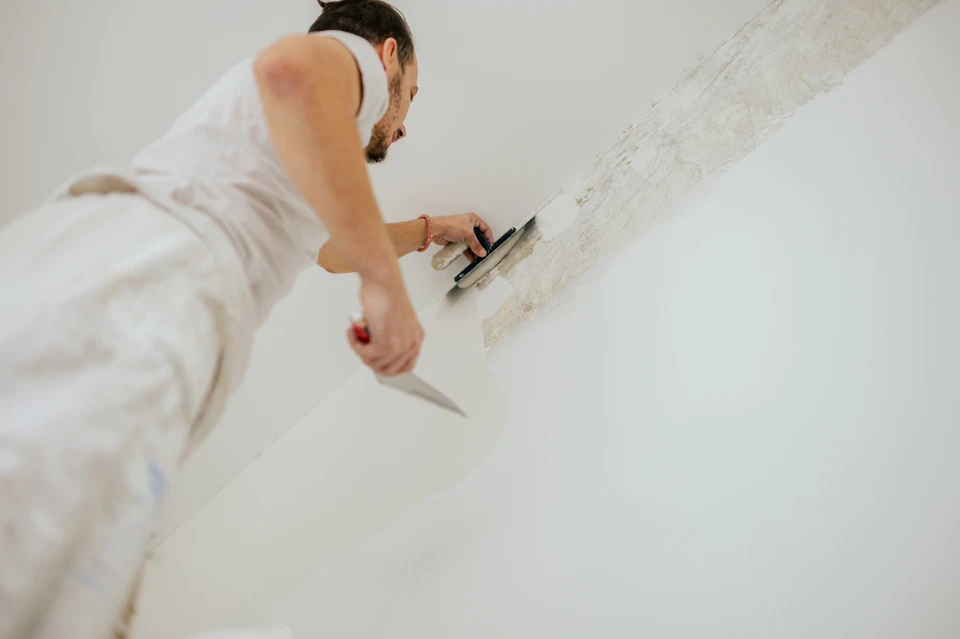 Vue en angle faible d'un plâtre sur l'échelle faisant du travail en plâtre et des murs de revêtement de finition pendant la rénovation de la maison